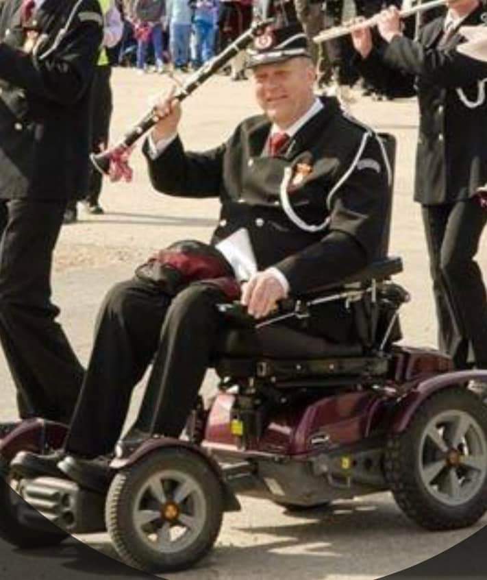 Viser uniformert mann i rullestol som spiller klarinett i 17.mai-tog